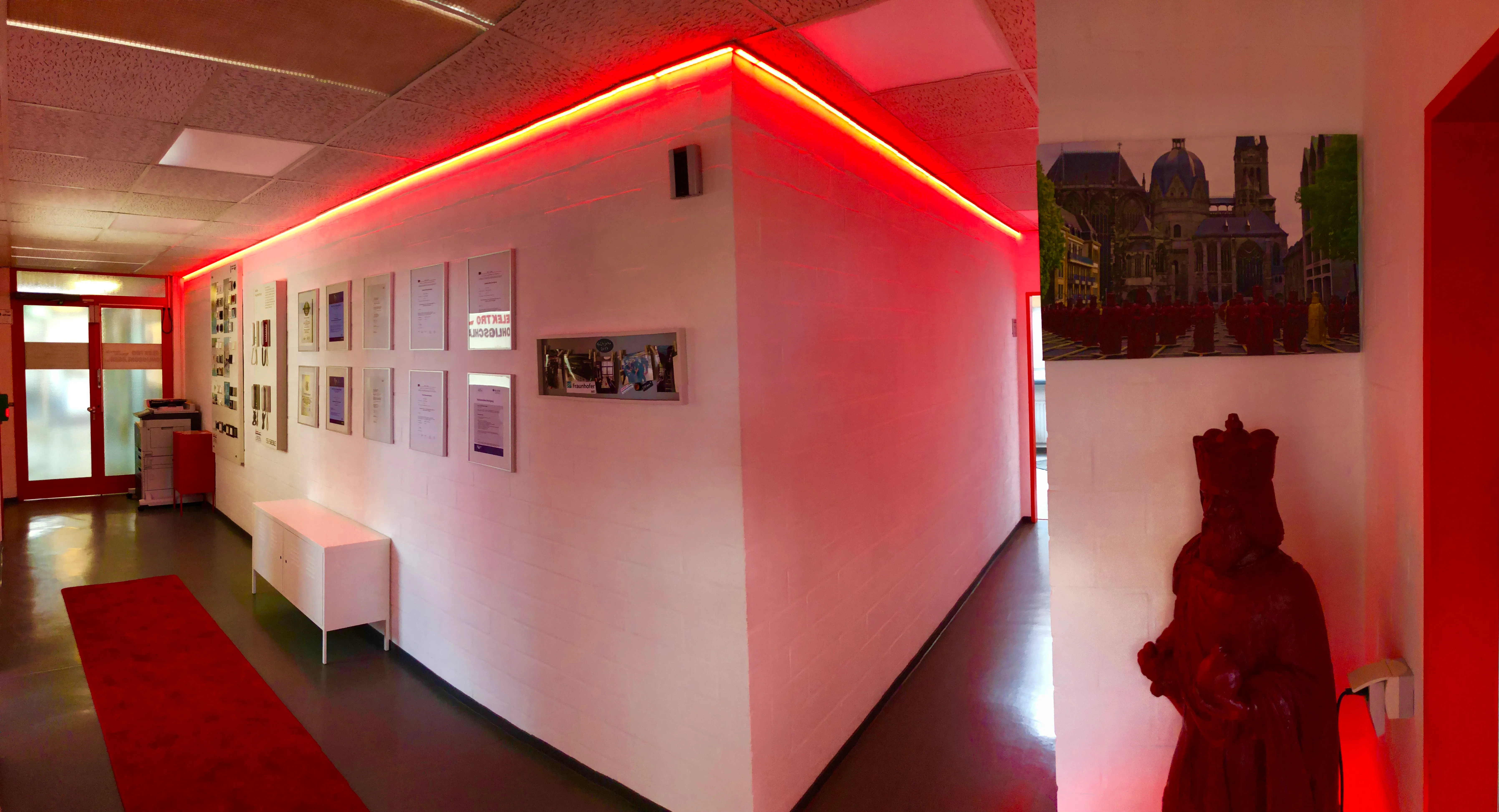 Innenansicht des Firmensitzes: heller Flur mit roter LED-Ambient-Beleuchtung und einer Wand mit Zertifikaten und Urkunden