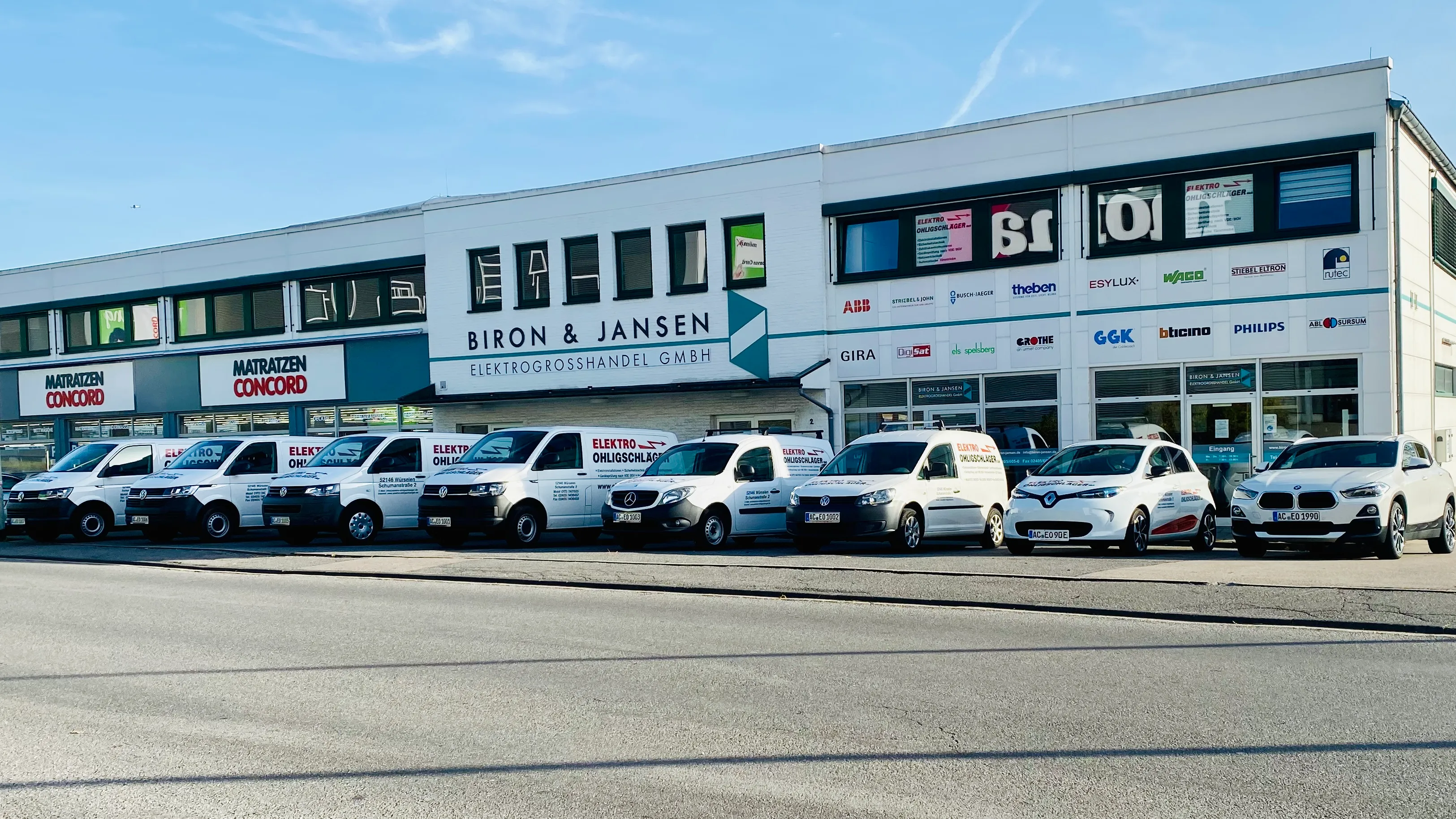 Acht Firmenfahrzeuge von Elektro Ohligschläger aufgereiht vor dem Firmensitz in Würselen im Jahr 2019